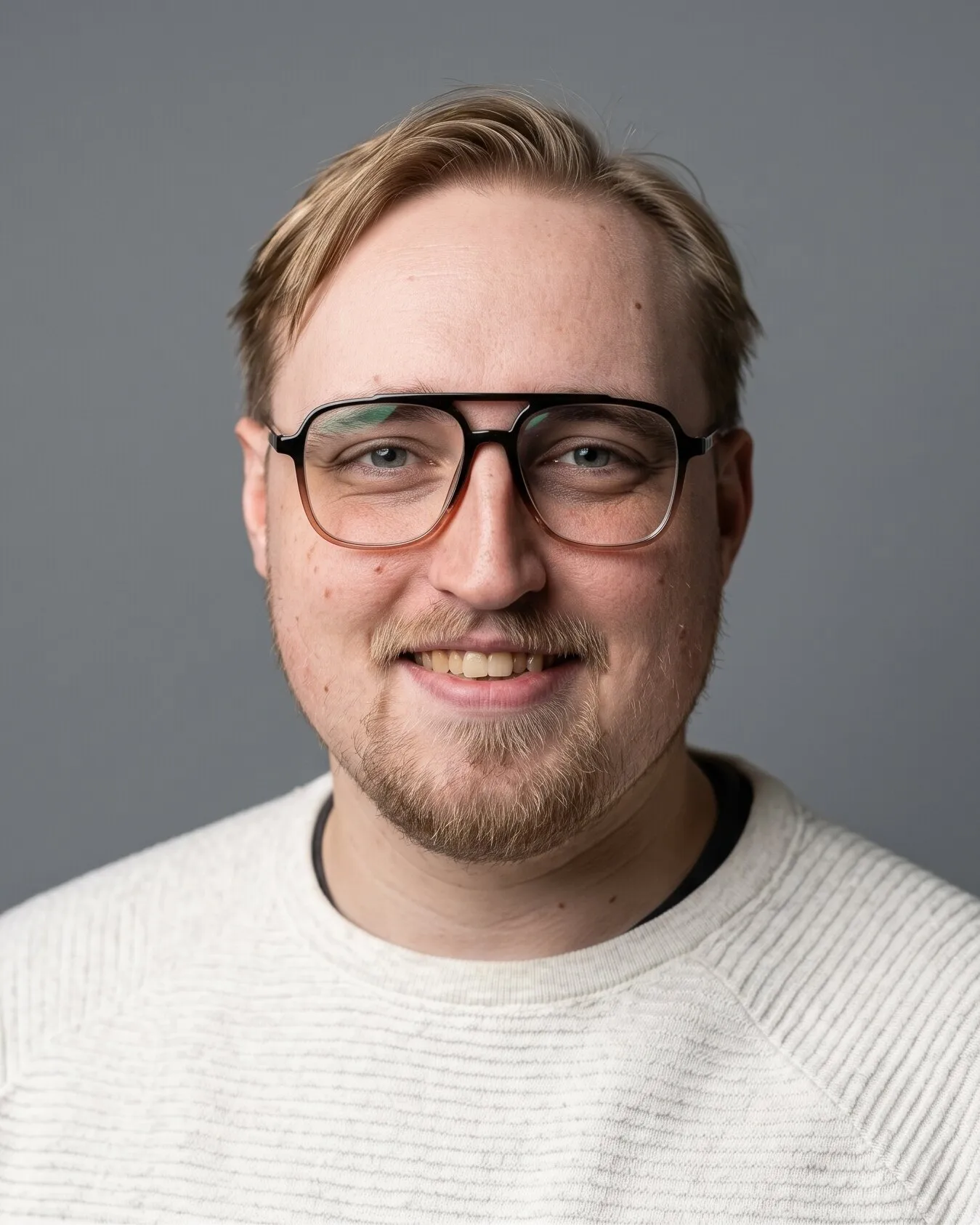 Ben Stanley, smiling, in glasses and a cream sweater against a gray backdrop